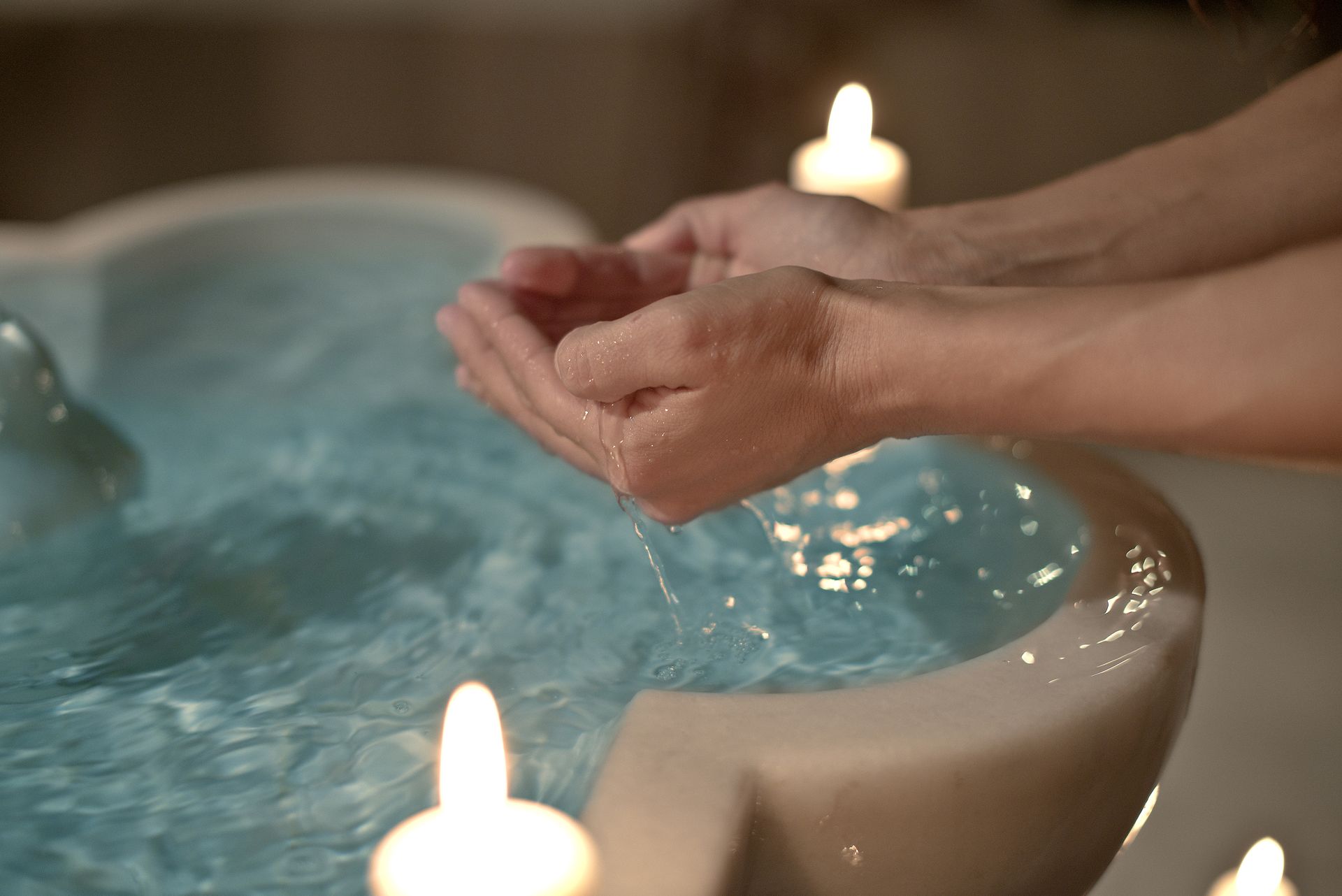 Manos recogiendo agua de una fuente de piedra iluminada por velas