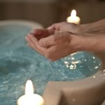 Manos recogiendo agua de una fuente de piedra iluminada por velas